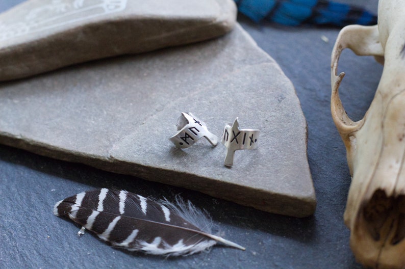 May include: Two silver rings with Roman numeral engravings. The rings are on a gray stone surface. The rings are in the shape of a bird with its wings spread.