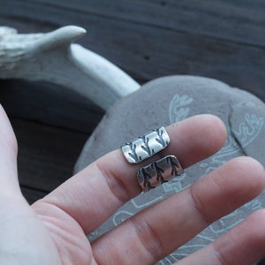 May include: Two silver rings with a textured design. The rings are worn on the index and middle fingers of a hand.