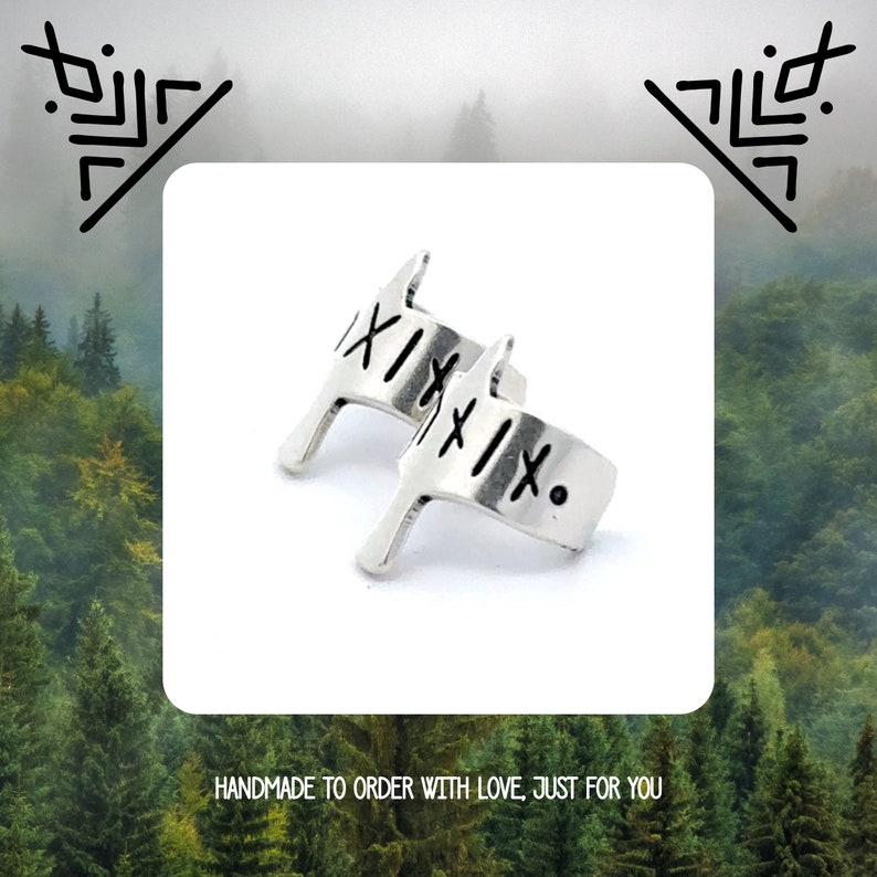 May include: Two silver rings with a unique design featuring the Roman numeral 'XI' engraved on each. The rings are handmade and have a minimalist aesthetic.