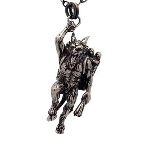 May include: Silver-toned pendant necklace featuring a detailed depiction of a horned, goat-legged figure carrying a basket and a torch. The pendant is suspended from a delicate chain, showcasing a gothic or mythological theme.