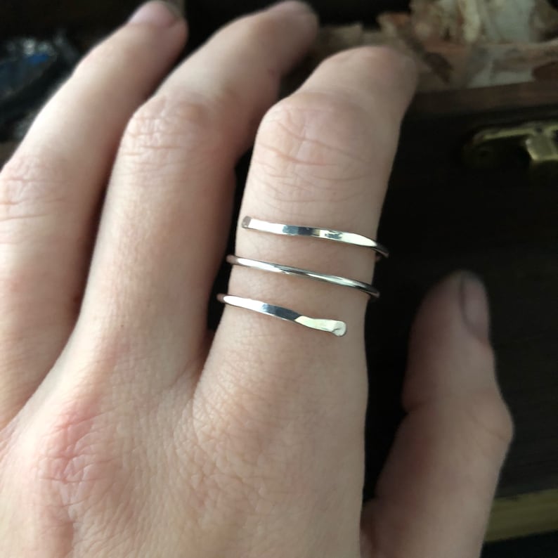 May include: A silver ring with three bands wrapped around each other. The ring is on a person's finger.