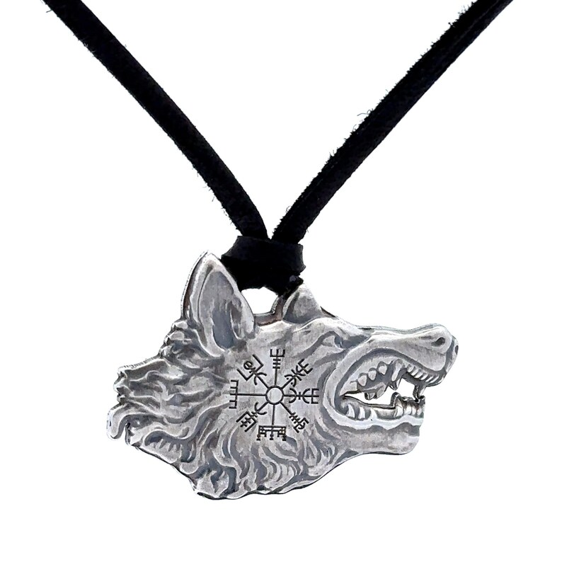 May include: Silver pendant necklace featuring a wolf head with a compass design and runes. The necklace has a black cord.