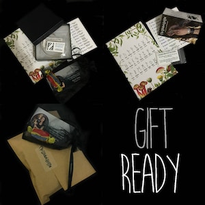 May include: A gift set with a variety of items, including a black pouch with a thank you note, a small black bag with a sticker that says "My Little Griffin", a white CD with a label that says "Blue Water Mermaid", a sheet of paper with a list of runes, and a sheet of paper with a list of words in a foreign language.