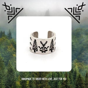 May include: Silver ear cuff with a design of a meditating figure with antlers surrounded by trees. The cuff is handmade and has a minimalist style.
