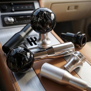 May include: A collection of car gear shift knobs and components. The knobs are black and white marbled spheres, and the components are silver and black. The items are arranged on a brown leather surface.