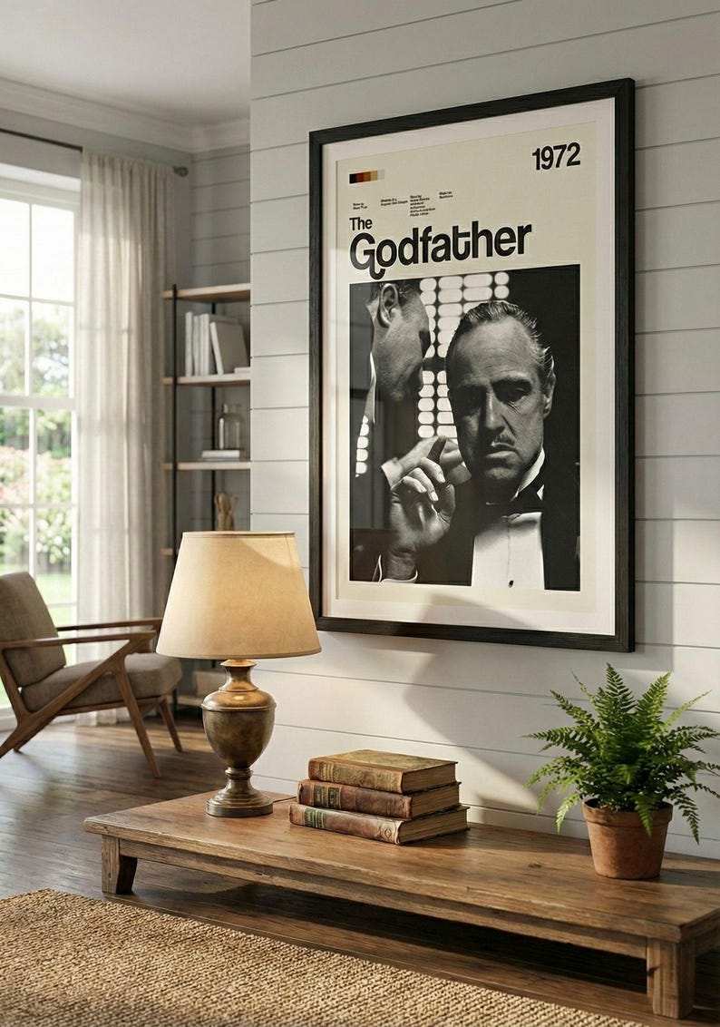 K&ouml;nnte beinhalten: Gerahmtes Schwarz-Wei&szlig;-Poster des Films "Der Pate" von 1972, das an einer wei&szlig;en Wand h&auml;ngt. Ein Holztisch mit B&uuml;chern und einer Lampe steht unter dem Poster. Eine kleine Topfpflanze steht auf dem Tisch.