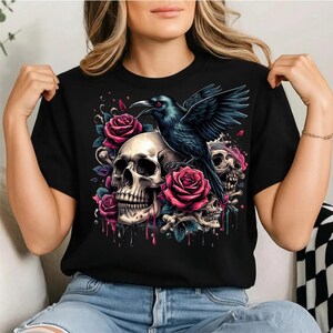 Puede incluir: Una camiseta negra de manga corta con un estampado gr&aacute;fico de un cuervo negro posado sobre un cr&aacute;neo humano. El dise&ntilde;o incluye rosas rosas y rojas vibrantes, calaveras m&aacute;s peque&ntilde;as y fragmentos de huesos con efectos de pintura que gotea.