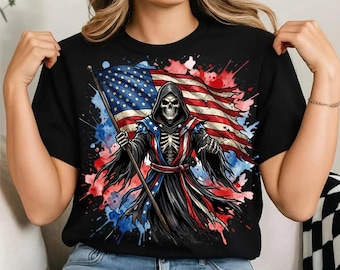 May include: A black t-shirt featuring a graphic print of a hooded skeleton figure holding a large American flag. The design includes red, white, and blue watercolor-style paint splatters surrounding the central figure, which wears a robe.