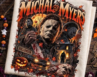 May include: A cream-colored t-shirt featuring a graphic print with the text MICHAL MYERS in orange dripping letters. The design includes multiple depictions of a masked figure, a jack-o'-lantern, a house, a car, and autumn leaves.