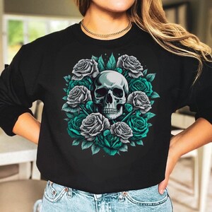 Puede incluir: Una sudadera negra de manga larga con un estampado gr&aacute;fico central de un cr&aacute;neo humano rodeado por una disposici&oacute;n circular de rosas grises y verde azulado con hojas verdes en la zona del pecho de la prenda.