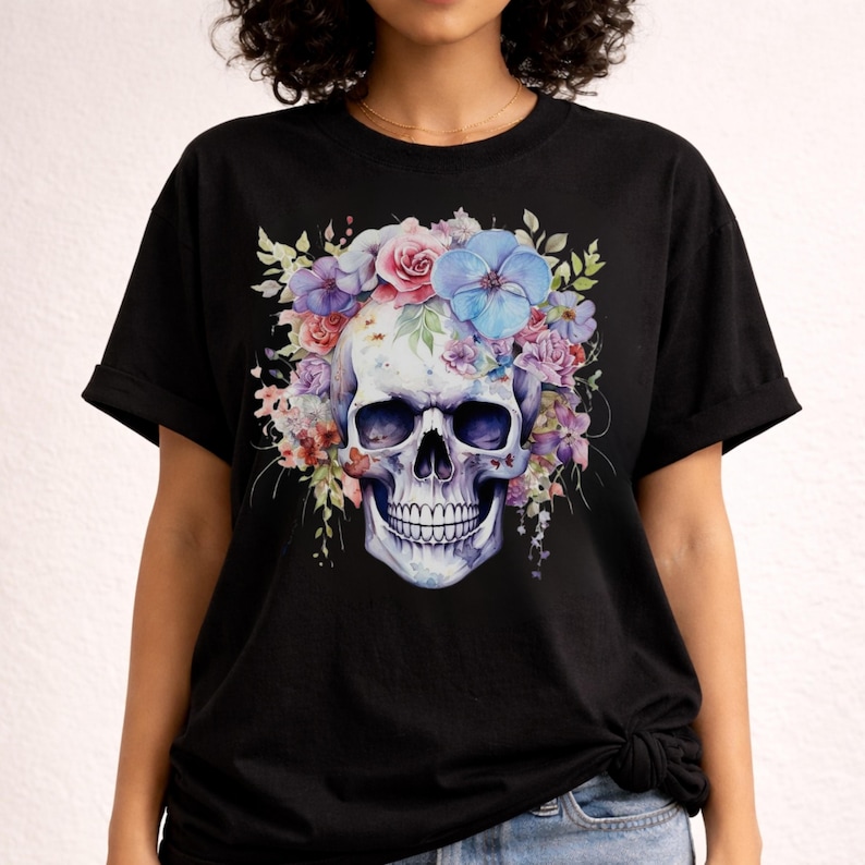 Puede incluir: Una camiseta negra de manga corta con un gr&aacute;fico central de un cr&aacute;neo humano adornado con una corona de flores en tonos acuarela vibrantes, incluyendo azul, morado, rosa y verde, situada en la parte frontal de la prenda de vestir.
