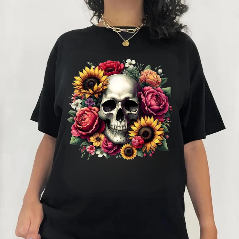 Puede incluir: Una camiseta negra con un gr&aacute;fico central de un cr&aacute;neo humano rodeado por un vibrante arreglo de flores coloridas, que incluye girasoles amarillos, rosas rojas y flores naranjas, creando un dise&ntilde;o floral detallado y contrastante.