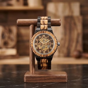 Può includere: Un orologio da polso con cinturino a maglie in legno bicolore e cassa circolare in legno. Il quadrante mostra un movimento meccanico scheletrato con ingranaggi dorati, numeri romani come indici delle ore e sottili lancette dorate.
