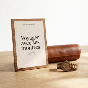 Puede incluir: Un letrero con marco de madera con el texto "WOODEN CROWN ART" y "Voyager avec ses montres PARTIE 8" en negro, un estuche de cuero marrón para relojes y un reloj de pulsera de madera con esfera redonda y correa de eslabones sobre madera.