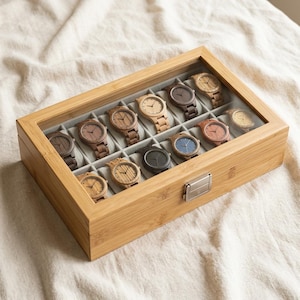 May include: A rectangular bamboo watch display case with a clear glass lid and a silver metal latch, containing twelve individual compartments. Each slot holds a wooden wristwatch with varying wood tones, dial colors, and link styles.