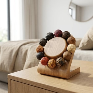 May include: A wooden display stand with a light wood finish, holding a bracelet of intricately carved, multi-colored beads. The beads are in shades of red, black, brown, and beige, with detailed patterns. The stand is on a wooden surface.