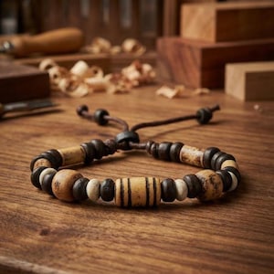 Peut inclure: Un bracelet de perles en bois avec un cordon en cuir marron. Le bracelet présente un mélange de perles en bois de différentes formes et couleurs, dont marron clair, marron foncé et blanc. Les perles sont enfilées pour créer un accessoire unique.