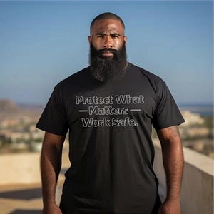 Może przedstawiać: Czarny t-shirt z napisem "Protect What Matters - Work Safe." Koszulka ma dekolt w serek i krótkie rękawy. Tekst jest biały, obramowany. Osoba na zdjęciu ma pełną brodę.