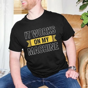Puede incluir: Camiseta negra de cuello redondo con el texto blanco y amarillo "IT WORKS ON MY MACHINE". La camiseta está hecha de un material suave y es adecuada para ropa casual. El diseño está centrado en el pecho.