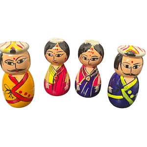 May include: Four hand-painted wooden dolls with rounded bodies and detailed facial features. The dolls are dressed in colourful traditional attire, including turbans and saris, in shades of yellow, red, and blue. The dolls are standing upright.