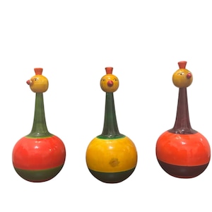 May include: Three handcrafted wooden bird ornaments. Each has a round body, a long neck, and a bird-like head with a red beak and a small red hat. The bodies are painted in red, yellow, and orange with green and brown accents.