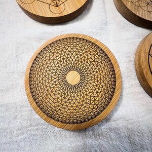 May include: A collection of round bamboo coasters with intricate geometric designs etched into the surface. The coasters feature a natural wood grain and a variety of patterns, including the Flower of Life and Metatron's Cube. These coasters are ideal for spiritual or bohemian home decor.