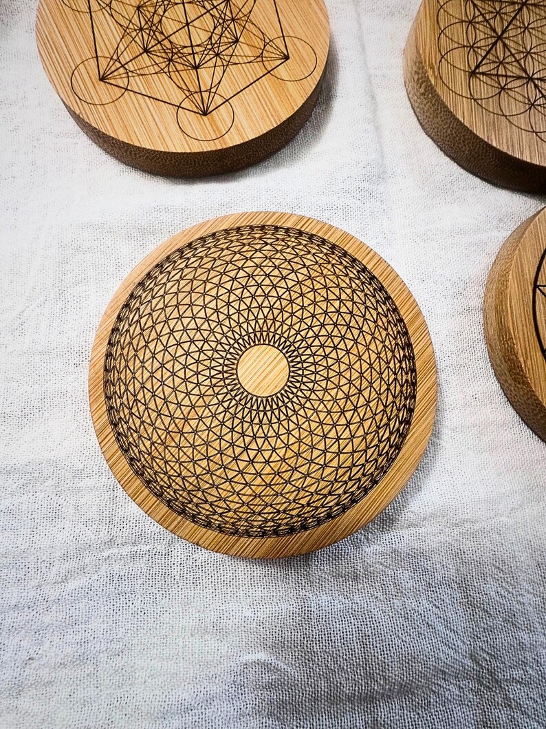May include: A collection of round bamboo coasters with intricate geometric designs etched into the surface. The coasters feature a natural wood grain and a variety of patterns, including the Flower of Life and Metatron's Cube. These coasters are ideal for spiritual or bohemian home decor.