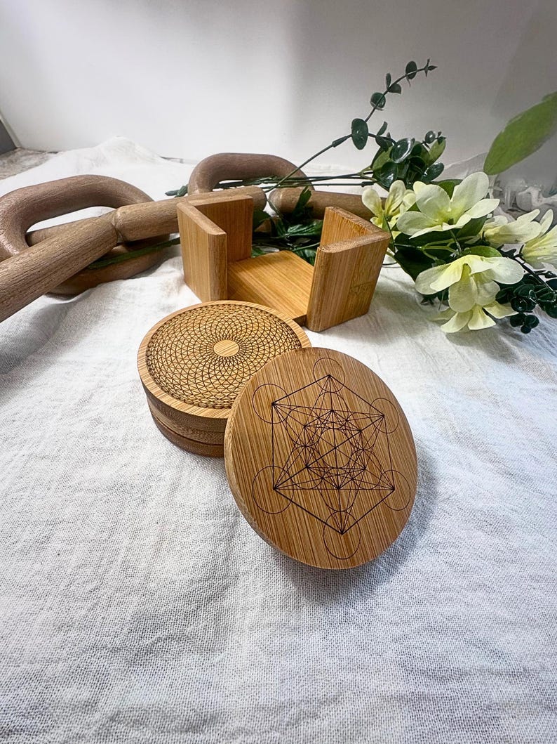 May include: A set of four round bamboo coasters with intricate geometric designs. One coaster features a Metatron's Cube pattern, while another displays a radial design. The coasters are stacked next to a bamboo holder.