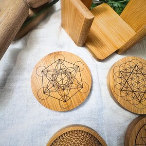 May include: A collection of bamboo coasters with geometric designs. The coasters feature intricate patterns, including the Metatron's Cube and other sacred geometry symbols. A bamboo holder and other bamboo items are also visible.