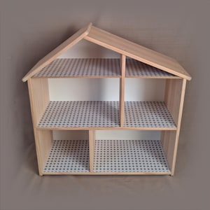 Peut inclure: Une maison de poupée en bois avec un toit en pente et plusieurs compartiments intérieurs. Les étagères sont recouvertes d'un papier à motifs avec un motif d'étoiles répétées en bleu et blanc. La maison de poupée est en bois clair.