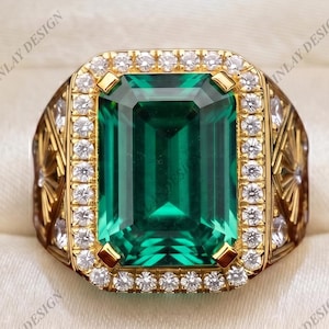 May include: A gold ring featuring a large emerald-cut green center stone surrounded by a halo of small white stones. The band displays intricate gold metalwork with geometric patterns and additional white stones on the sides, presented in a box.