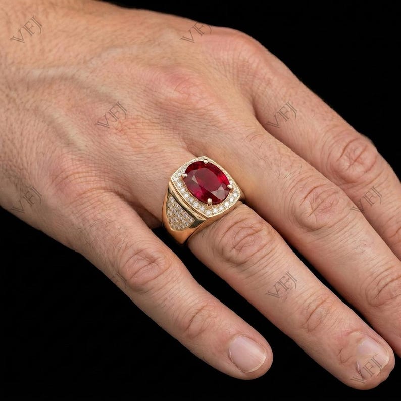 May include: A gold ring featuring a large, oval-cut red gemstone set in the center, surrounded by a halo of small, clear pav&eacute;-set stones. The band is wide and also encrusted with multiple small, clear stones along the sides of the setting.