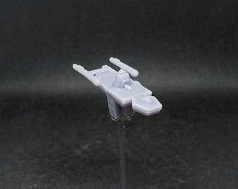 Pode incluir: Um pequeno modelo de nave espacial em resina cinzenta sem pintura, com um casco central, uma secção de ponte elevada e duas gôndolas de motor paralelas que se estendem da parte traseira. A miniatura está montada numa haste vertical fina.