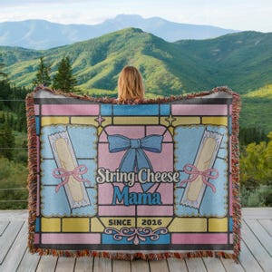 May include: A colorful throw blanket with a stained-glass design. The blanket features the text "String Cheese Mama" and "Since 2016". The design includes images of string cheese, bows, and a decorative border. The blanket is fringed.