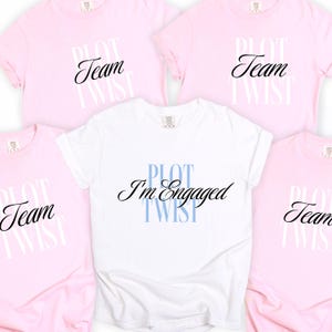 May include: Five t-shirts, four pink and one white, with the words "Team Twist" and "Plot I'm Engaged Twist" printed on them. The text is in a mix of cursive and block letters. The shirts are short-sleeved.