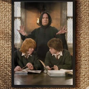 May include: A framed print featuring a scene from a movie. The image shows three people, with one person standing behind two others. The two people in front are seated at a table. The print is in a black frame.