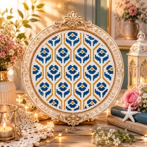 May include: A circular cross-stitch embroidery piece featuring a repeating geometric pattern of blue and yellow flowers on a white fabric background, encased in an ornate, cream-colored, vintage-style frame with intricate scrollwork details.