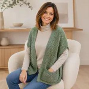 May include: A sage green sleeveless knit vest featuring a textured stitch pattern and two large front patch pockets. The vest is worn over a beige long-sleeved mock neck top and blue denim jeans, creating a layered look with a relaxed fit.