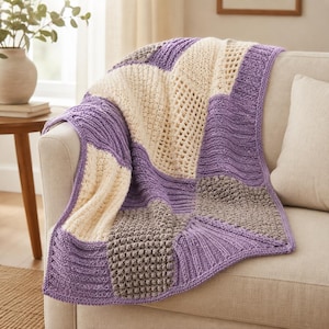 May include: A knitted throw blanket featuring a patchwork design of square panels in shades of lavender, cream, and taupe. The blanket displays various textures including ribbed, bobble, and open-work knit patterns, creating a tactile surface.