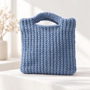 Peut inclure: Un sac à main en crochet bleu pervenche de forme carrée, doté d'un motif en maille côtelée épaisse et texturée ainsi que d'une poignée intégrée sur le dessus. Le sac présente une silhouette structurée et carrée avec un tissage uniforme.