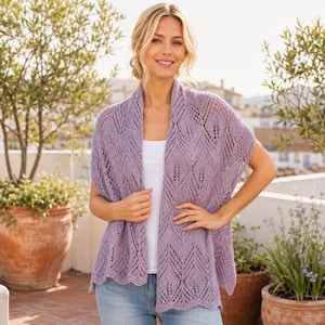 May include: A light purple, open-front knit cardigan featuring a delicate, repeating chevron and leaf-like lace pattern. The garment has a scalloped hemline and is worn over a plain white top and light blue denim jeans.