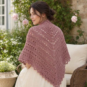 May include: A dusty rose triangular crochet shawl featuring an intricate openwork pattern with repeating geometric lines and a scalloped edge. The shawl is draped over the shoulders, showcasing the textured yarn and the detailed stitch work.
