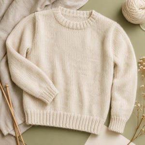 May include: A cream-colored long-sleeve sweater featuring a classic crew neckline and ribbed cuffs and hem. The garment is crafted with a chunky knit texture, showcasing a solid, neutral tone throughout the entire piece of knitwear.