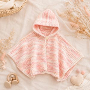 Può includere: Un poncho con cappuccio lavorato a maglia in filato variegato con delicate sfumature di rosa e bianco. Il capo presenta una chiusura con un singolo bottone sullo scollo, una trama a coste su tutto il corpo e un cappuccio a punta con orlo.