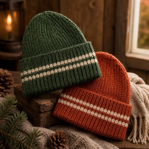 Peut inclure: Un bonnet en tricot vert foncé et un bonnet en tricot orange brûlé, tous deux dotés d'une texture côtelée et de deux rayures horizontales couleur crème sur le revers. Les bonnets sont fabriqués avec un fil épais et une forme arrondie.