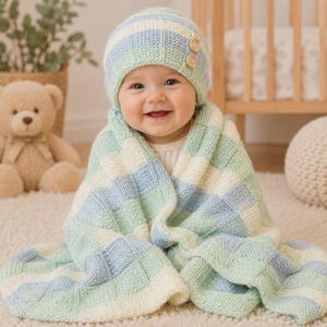 May include: A knitted baby hat and matching blanket featuring a checkered pattern in soft shades of light blue, mint green, and cream. The hat is adorned with three small, round, light brown wooden buttons on the side, adding a subtle texture.