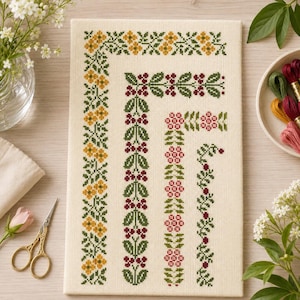May include: A rectangular piece of cream-colored Aida fabric featuring four vertical cross-stitch borders. The patterns include yellow flowers, dark red berries with green leaves, pink flowers, and a thin vine with small red berries.