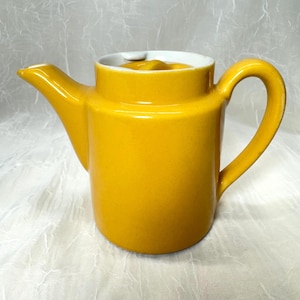 Peut inclure: Une théière en céramique jaune vif avec un bec verseur incurvé et une grande anse arquée. Le bord intérieur est blanc. La théière est de couleur unie et a une finition brillante. La théière est conçue pour servir le thé.