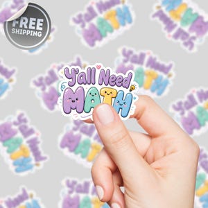 Könnte beinhalten: Ein farbenfroher Aufkleber mit dem Text "Y'all Need MATH" in einer verspielten Schriftart. Das Wort "MATH" ist in Pastellfarben mit niedlichen Gesichtern gehalten. Eine Hand hält den Aufkleber, mit anderen ähnlichen Aufklebern im Hintergrund.