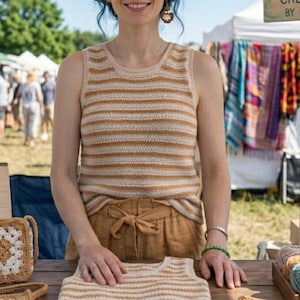 Puede incluir: Un top de ganchillo a rayas color crema y beige. El top sin mangas se exhibe en una persona en un mercado al aire libre. Un top de ganchillo a juego está sobre la mesa. La persona lleva pantalones color beige. Un bolso de ganchillo está sobre la mesa.